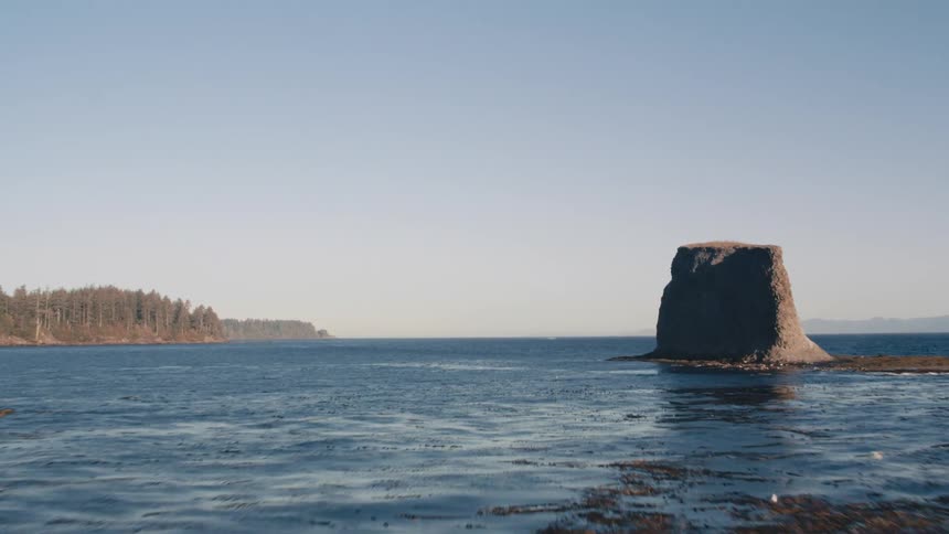 Aerial landscape of large rocks in the middle of the ocean and a mountainous forest in the background