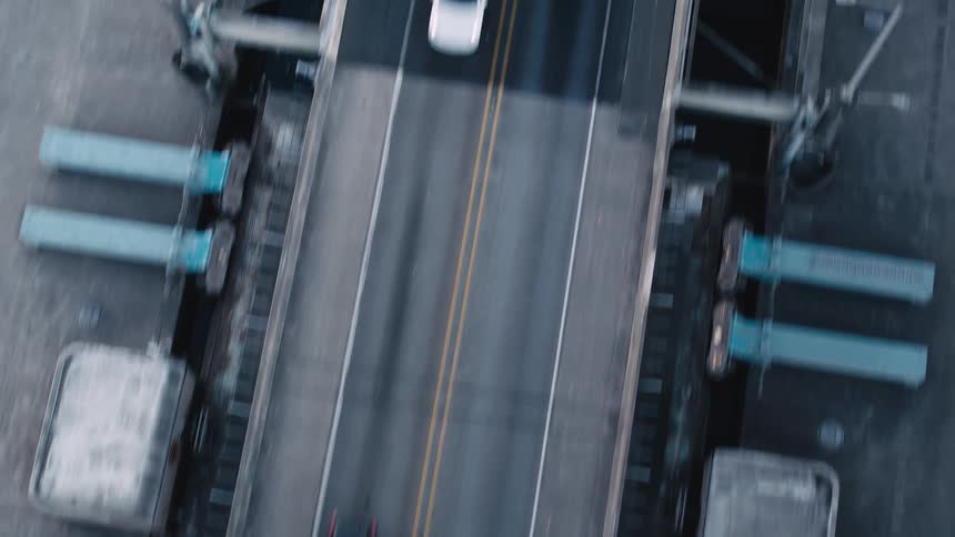 A straight asphalt road over a bridge with double yellow lines bisects a dark still body of water viewed directly from above