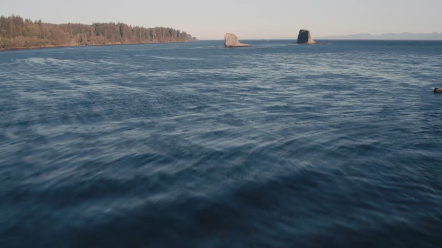 A fastmoving revealing aerial shot shows the ocean whizzing by approaching large rocks in the water and distant coast