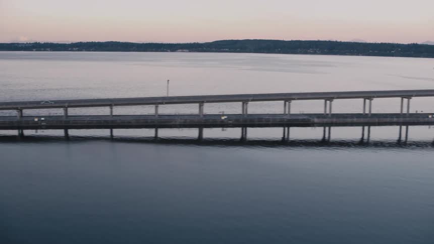 The hood canal bridge floats on calm waters framed by distant mountains and a twilight sky