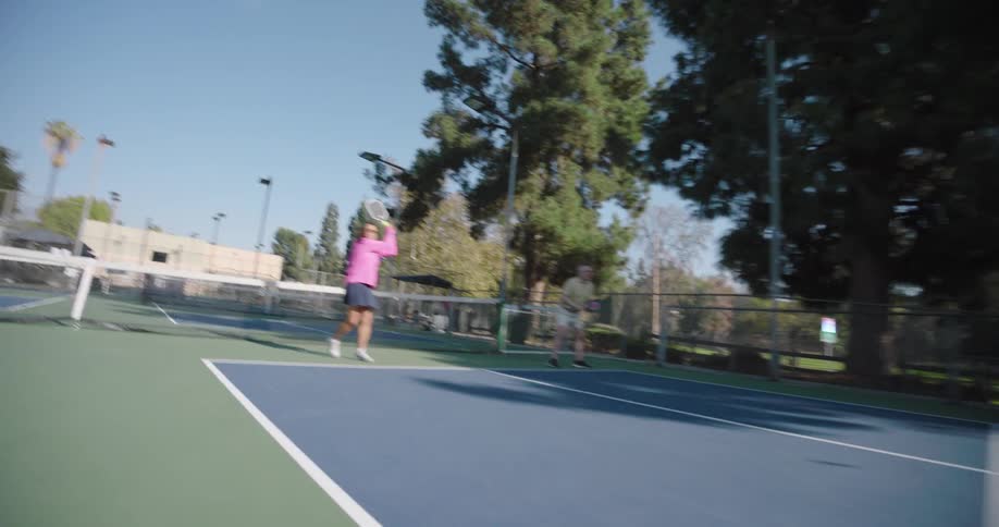 Two couples playing pickleball on an outdoor court surrounded by tall trees and a fence