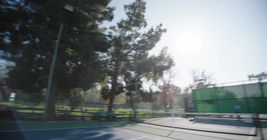 People play pairs pickle ball on a court in the park on a sunny day