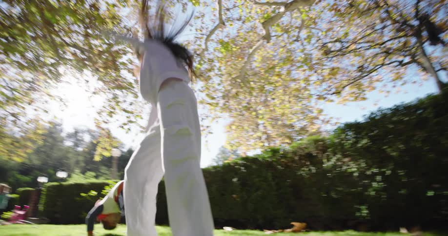 Two children are playing on a grassy lawn with one child performing a cartwheel and the other child rolling over