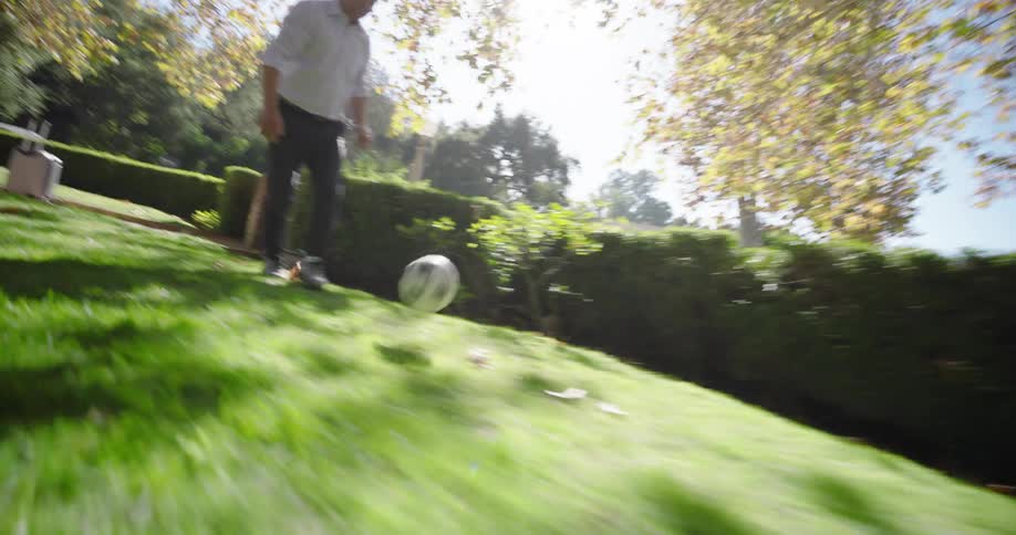 A father and his daughter playing soccer on a grassy lawn on a sunny day