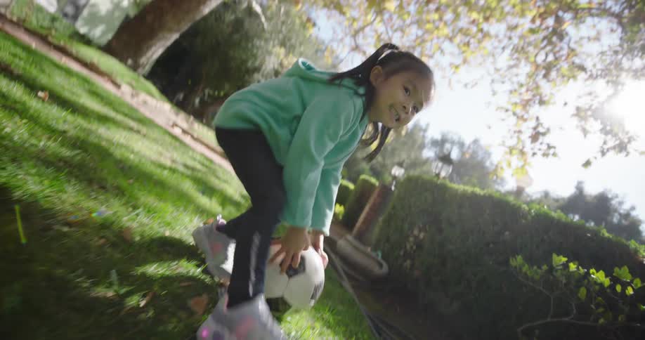 Father and daughter play with a soccer ball in their yard under a large tree on an autumn day