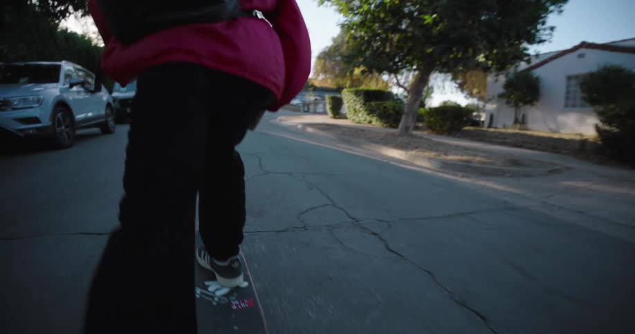 A skateboarder with a backpack and beanie rides down a residential street