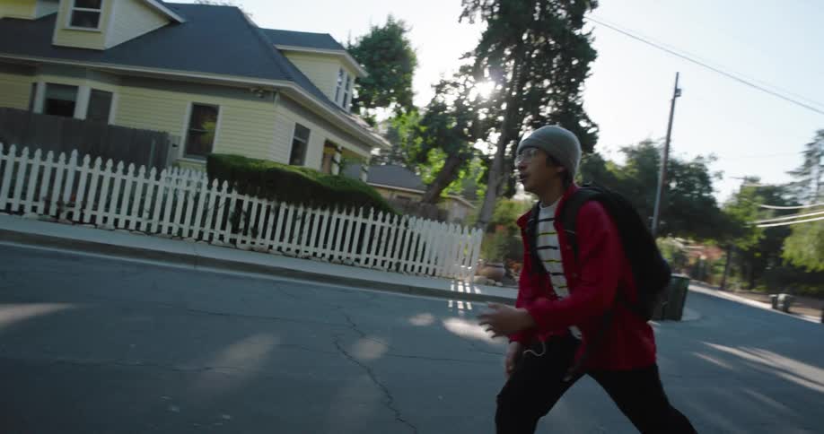 A teenager wearing a red jacket and black pants skateboards on a residential street