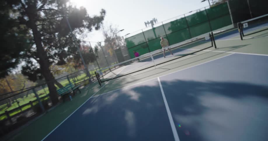 Two couples playing pickleball on an outdoor court surrounded by tall trees and a fence