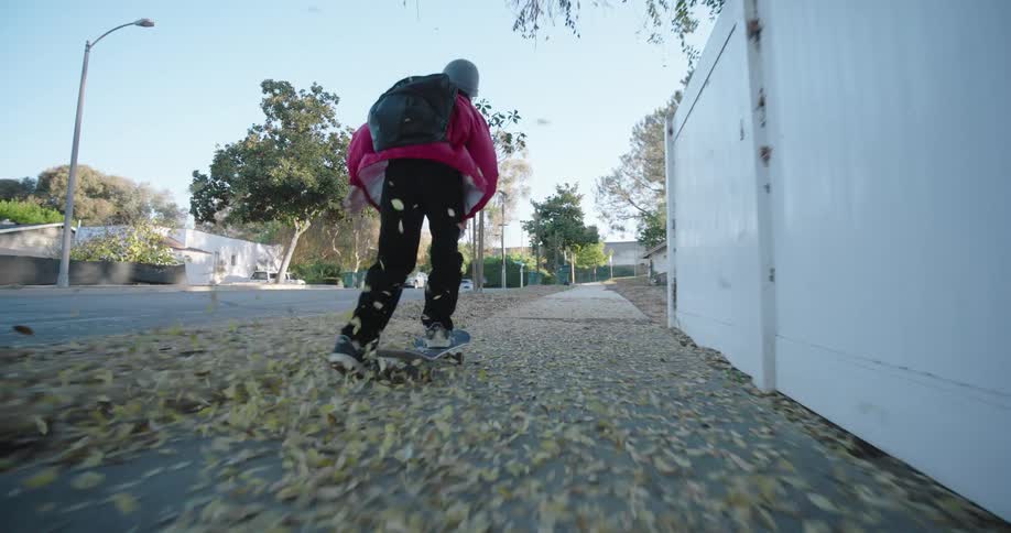 A boy skateboards through the leaves on the sidewalk