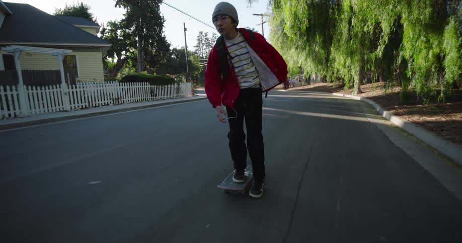 A teenage boy rides a skateboard on a residential street on a sunny day