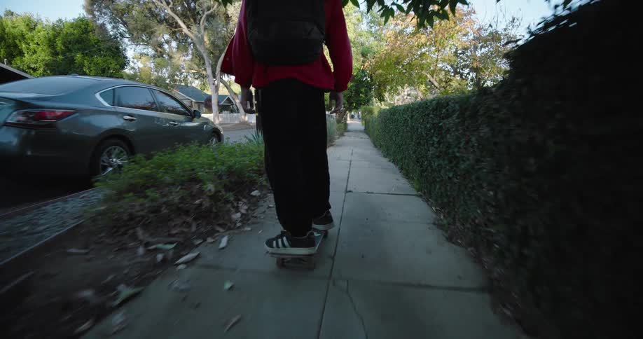 A teenager wearing a red jacket and black pants skateboards on a residential street