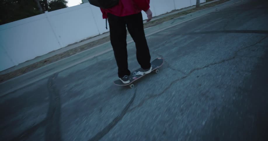 A teenage boy rides a skateboard on a residential street on an autumn day