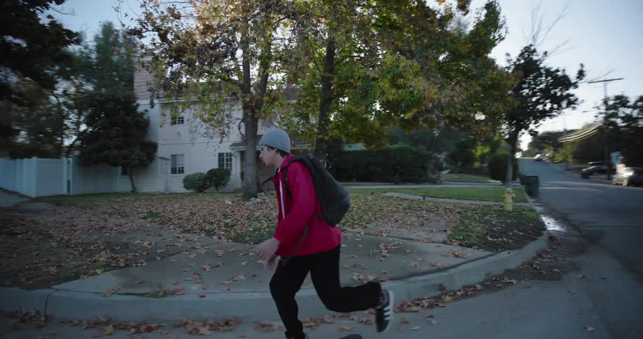 A teenager wearing a red jacket and black pants skateboards on a residential street