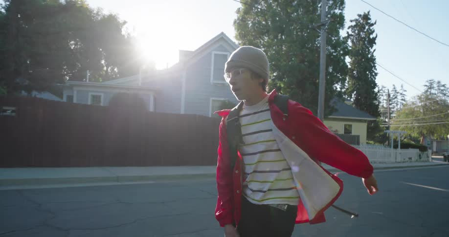 A teenager wearing a red jacket and black pants skateboards on a residential street