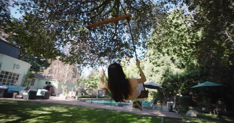 A girl is swinging on a rope swing attached to a large sturdy tree branch in a sunlit garden
