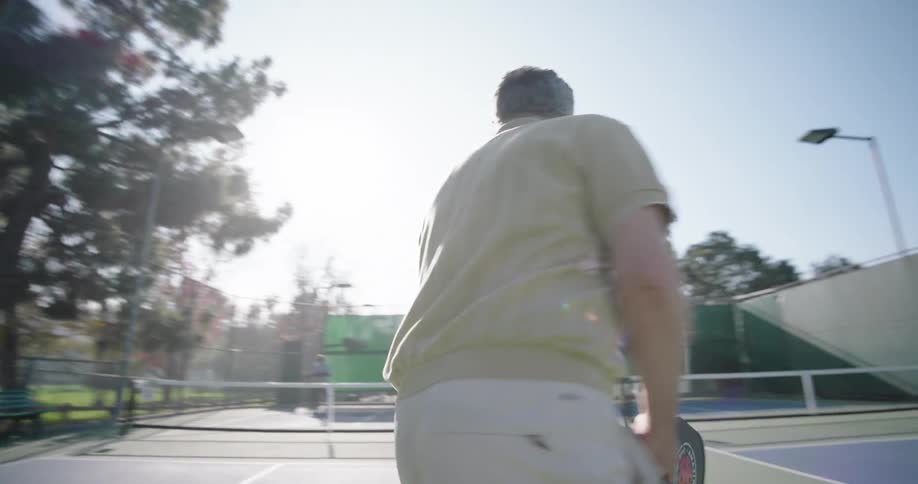 Two couples playing pickleball on an outdoor court surrounded by tall trees and a fence