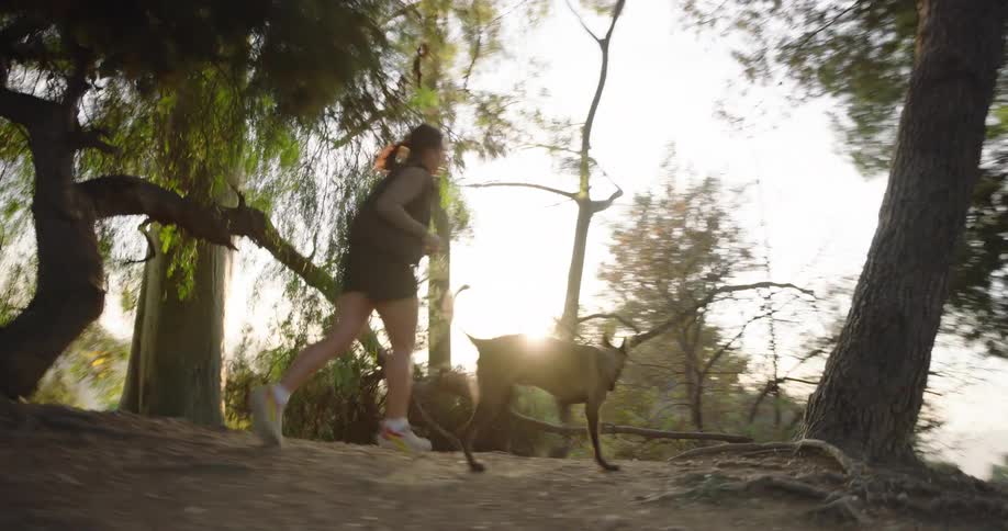 Woman runs along a path through the woods with her dog