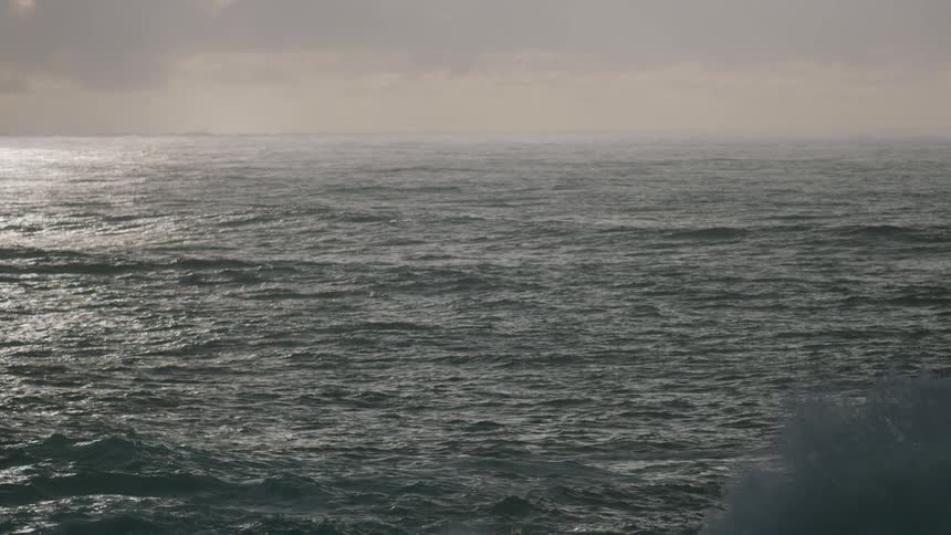 A vast calm ocean stretches out under a cloudy sky with the horizon barely visible in the distance