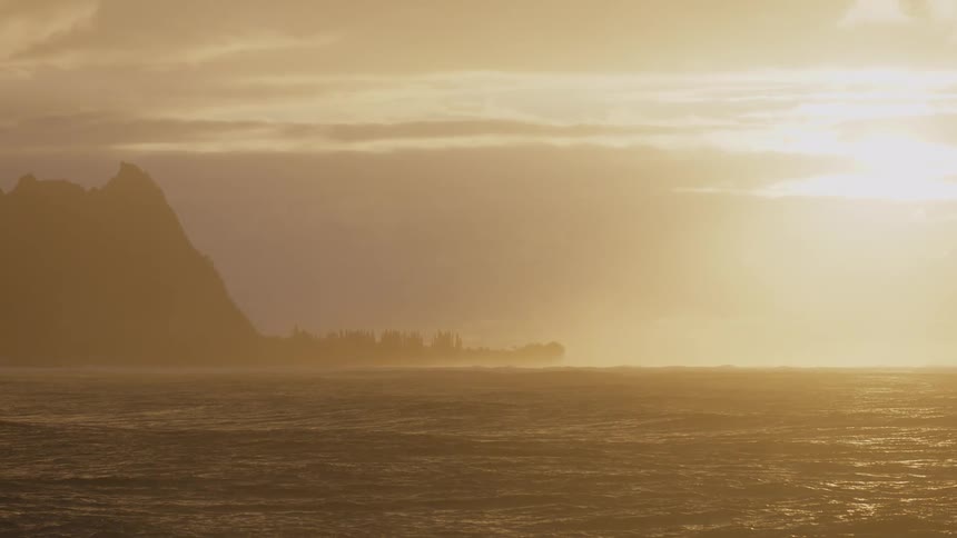 Sun glares from a red tinted horizon on to a foggy coast on a cloudy day