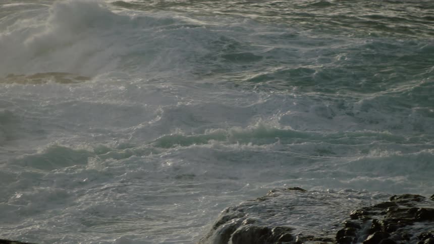 Turbulent ocean waves crash against rocks creating a flurry of white foam and powerful motion