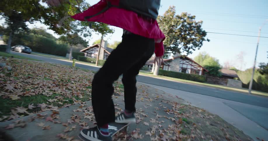 A teenager wearing a red jacket and black pants skateboards on a residential street
