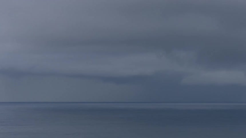 The dark still ocean meets a heavy overcast sky in a somber landscape