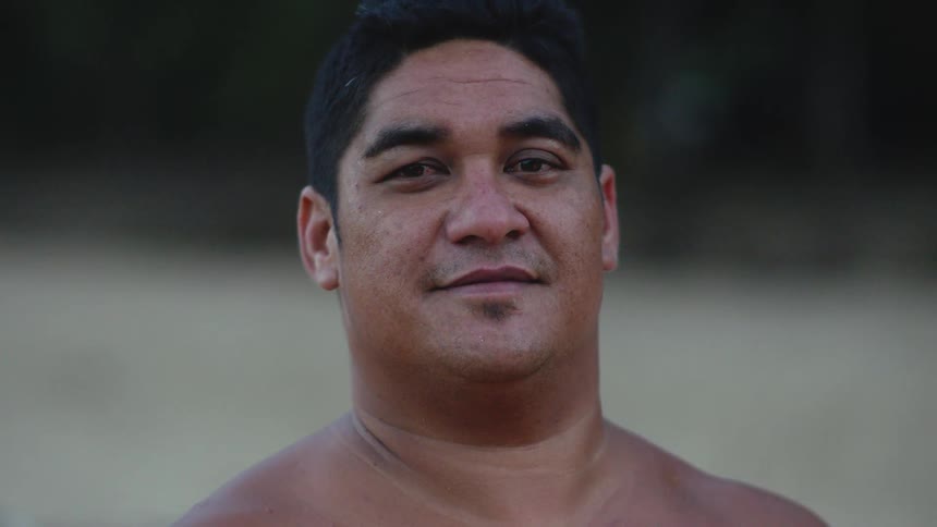 Man is standing shirtless looking forward with very little expression