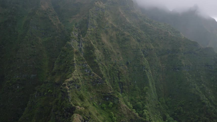 A lush steep mountain range with rugged terrain and dense vegetation is partially shrouded in mist