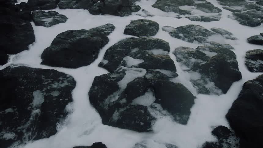 Dark jagged rocks partially covered by white sea foam