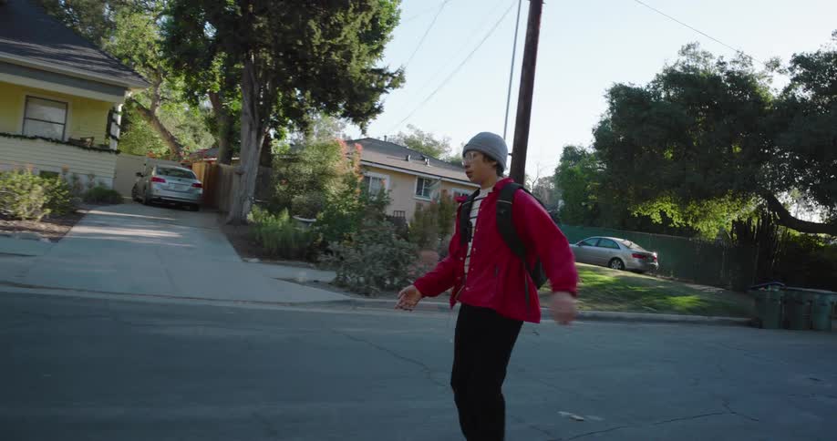 A teenage boy skateboards on a residential street on a sunny summer day