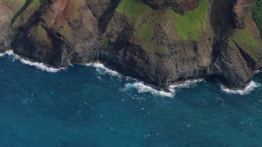 Waves crash against a rocky shore creating white foam in the blue ocean water