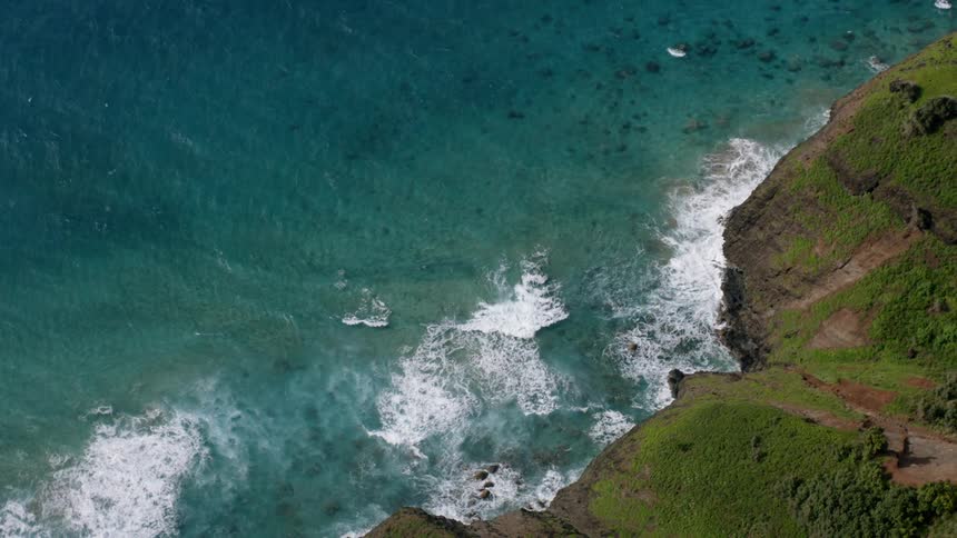 Ocean waves crash against a green rocky cliffside