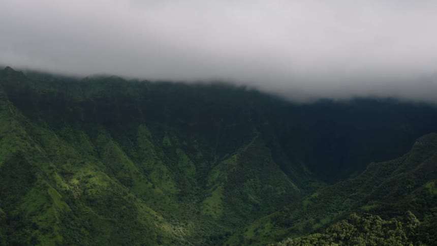 Jagged green cliffs rise steeply their peaks disappearing into a thick lowhanging fog that obscures the upper portions of the rugged terrain