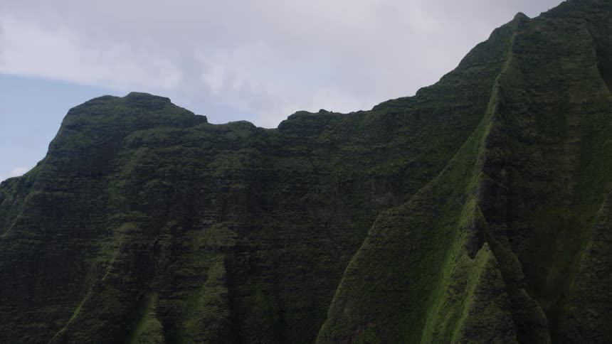 An aerial view shows steep green mountain slopes and cliffs