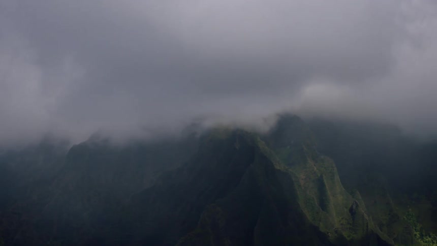 Jagged mountain peaks rise against a misty overcast sky obscured by swirling clouds