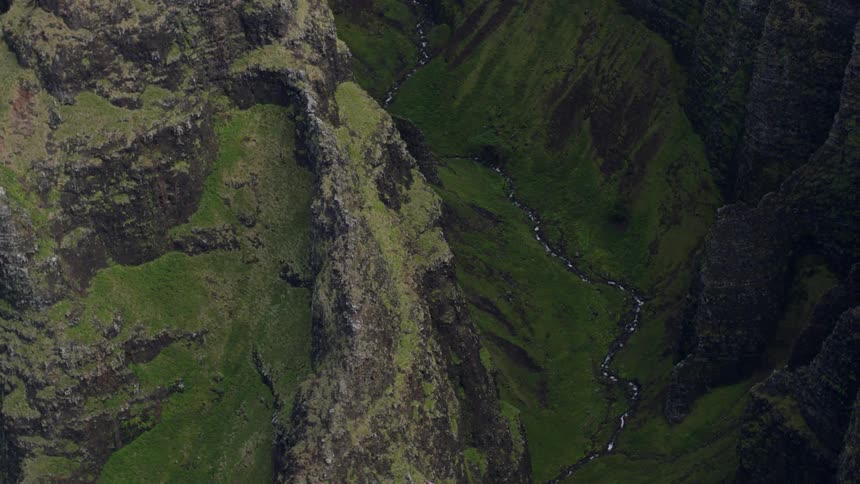 A narrow stream winds through a deep rocky gorge covered in patches of green moss and vegetation