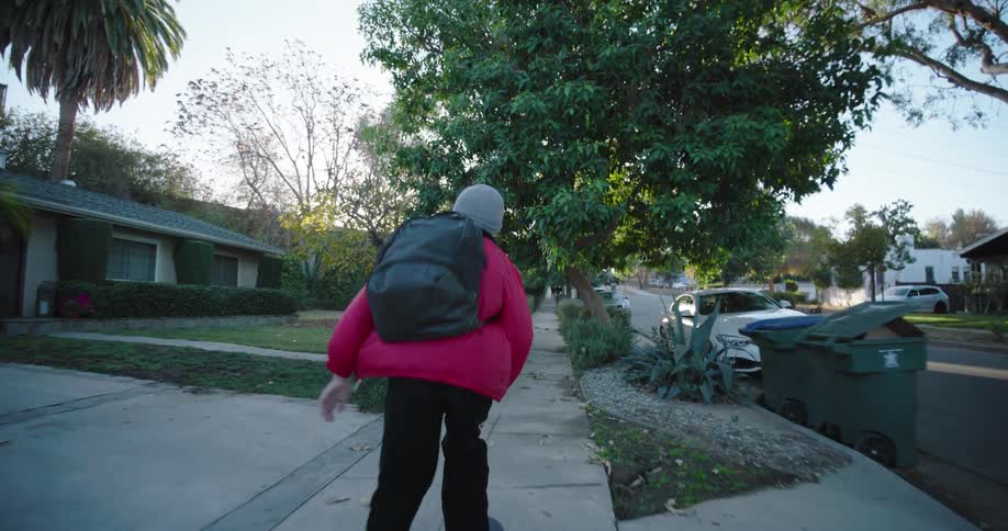 A teenager wearing a red jacket and black pants skateboards on a residential street