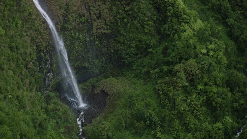 Multiple waterfalls flow down a vegetation covered slope and into a narrow stream
