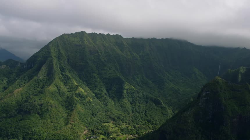 A panningright aerial view shows a vast lush green mountain landscape with steep slopes and valleys