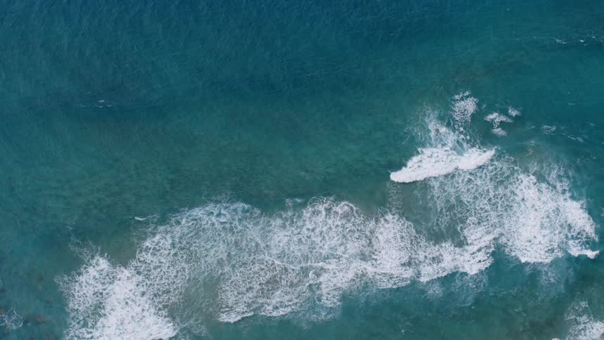 Crashing waves create a white textured pattern against the dark blue surface of the ocean