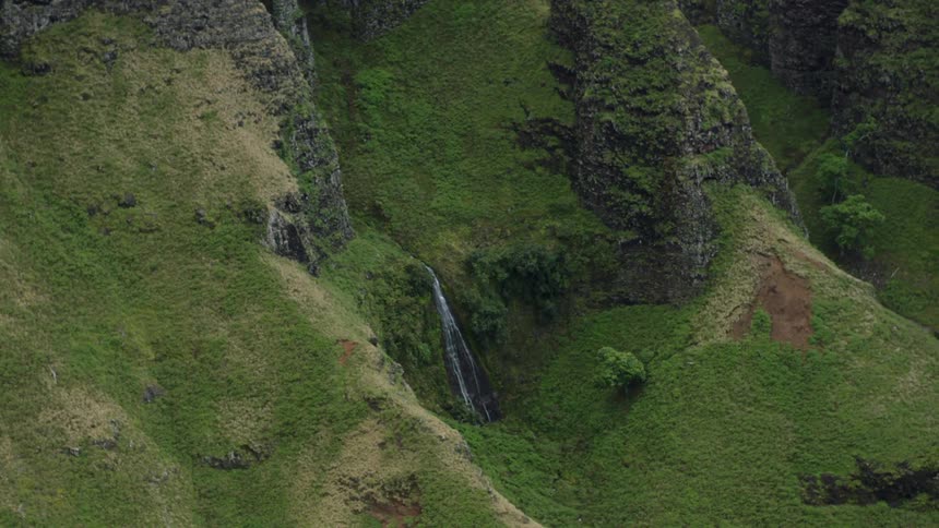 A view of steep green cliffs shows a thin waterfall cascading down the mountainside