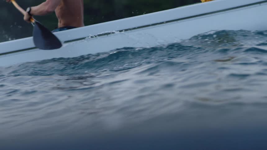 Two people are rowing a boat on a body of water with the focus on their arms and oars as they cut through the water