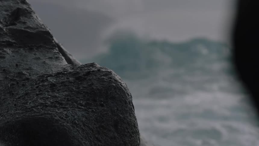 Rough ocean wave seen through rocks in foreground