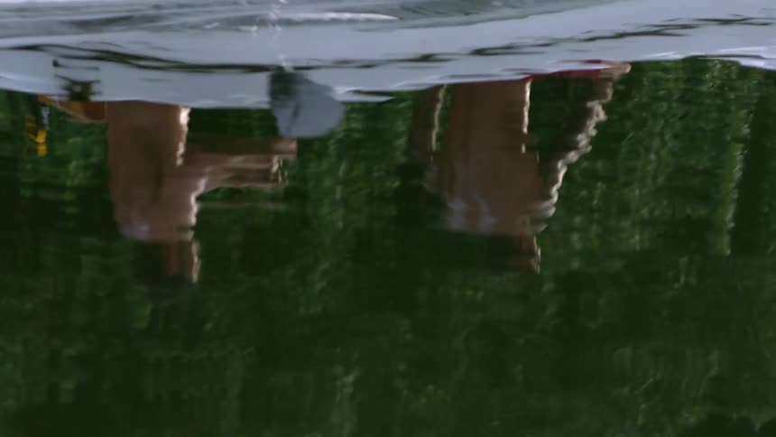 Reflection of two men rowing a boat across a lake