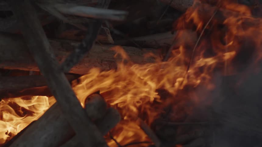 Flames lick at dry stacked branches creating a bright orange glow against a dark background