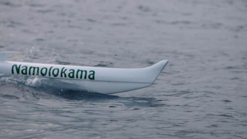 The white hull of a sailboat juts into rippling water