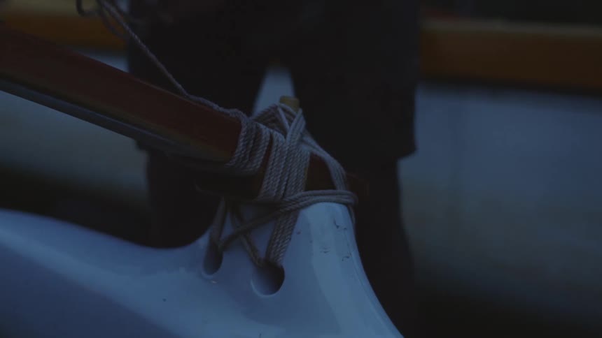 Close up of a person untying a rope from a boat at twilight