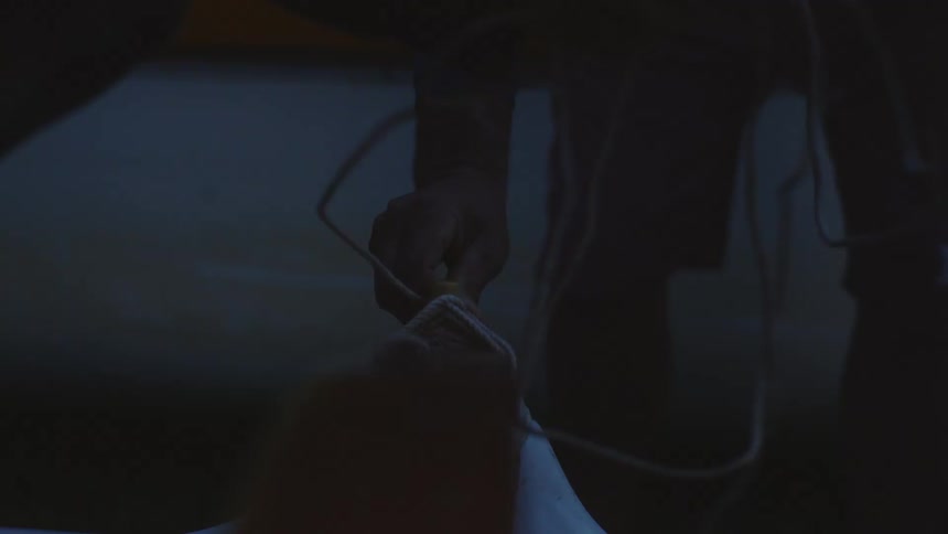 Man stabilizes a wooden item while another man unwraps a cord