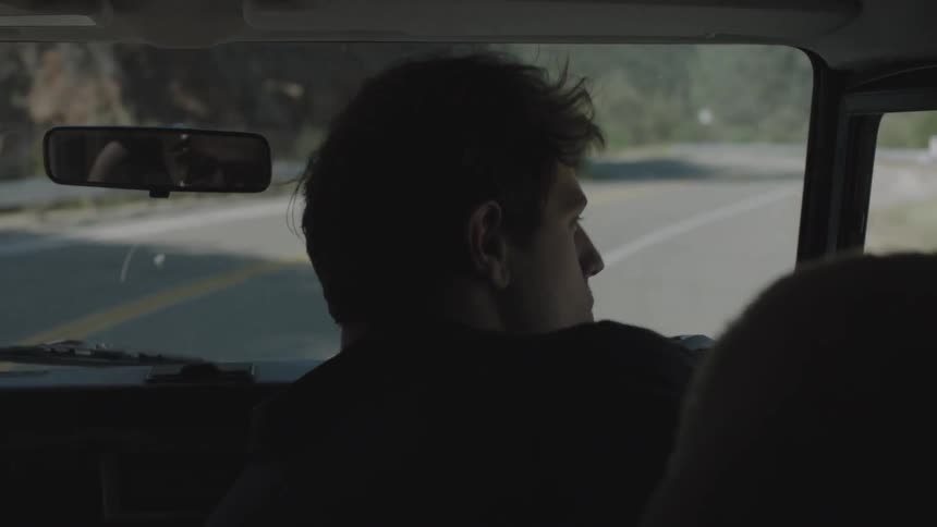 A man taking photographs out of a vehicle window as another person drives along a winding road