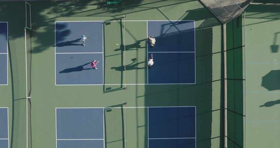 An aerial view of a doubles pickleball game in progress with two players on each side of the net casting long shadows on the court